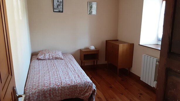 Een kleine, eenvoudig ingerichte kamer met een bed, nachtkastje, houten kast en radiator.