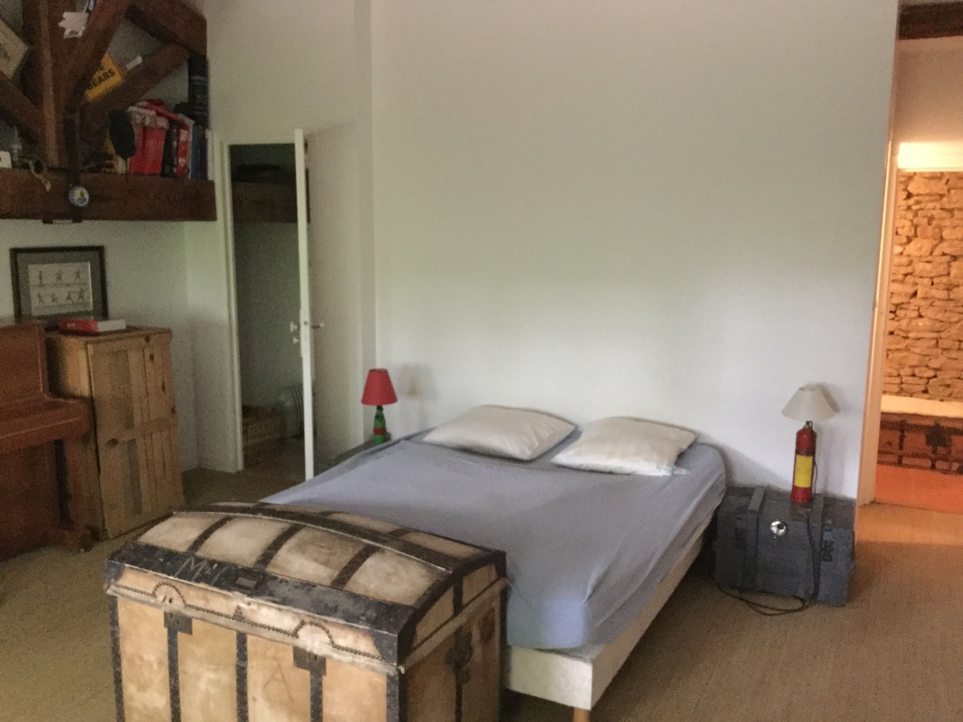 A bedroom with a bed, a suitcase, a lamp, and a stone wall.