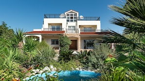 Un edificio de dos pisos con balcones, piscina y abundante vegetación.