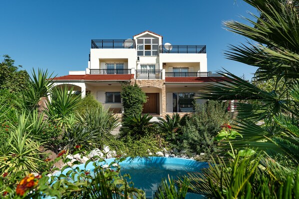 A two-story building with balconies, a swimming pool, and lush greenery.