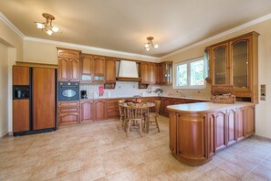 A kitchen with wooden cabinets, a central island, a dining table with chairs, and a built-in oven.