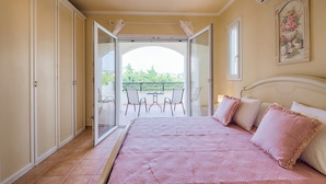 Un dormitorio con cama, un balcón con sillas y un cuadro en la pared.