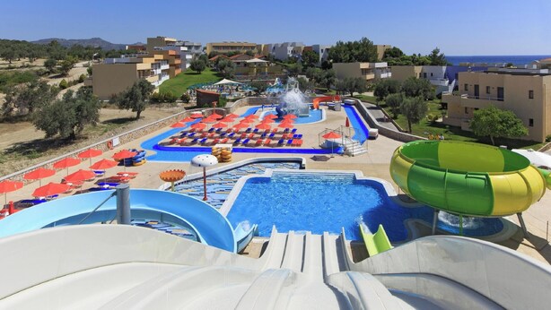 Un parque acuático con múltiples toboganes y piscinas, rodeado de edificios y un cielo despejado.