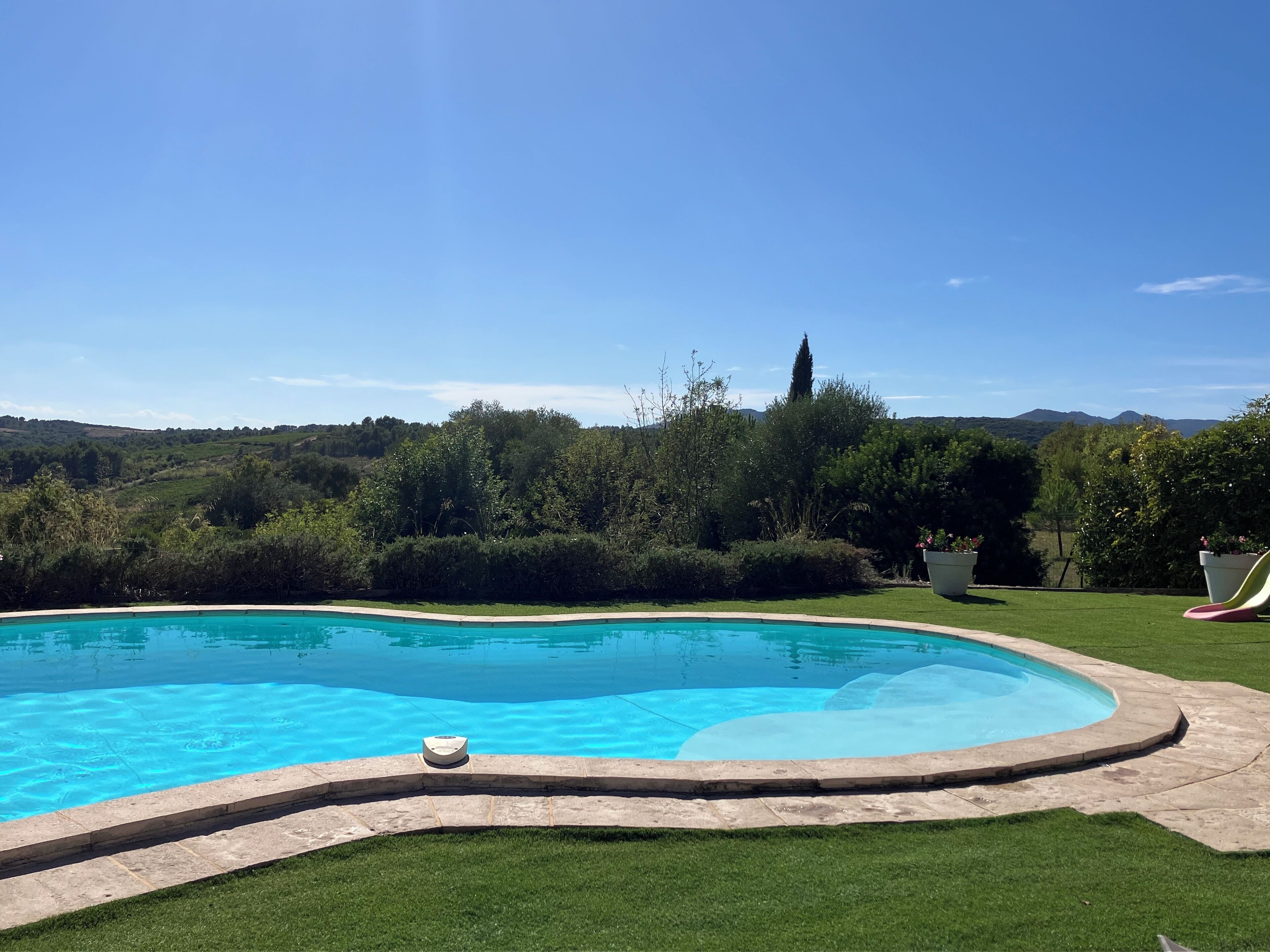 Una piscina con bordatura in pietra, circondata da prato curato e alberi, con vista panoramica su colline lontane.