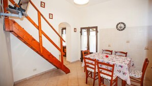 A dining area with a wooden staircase, a dining table with chairs, and a clock on the wall.