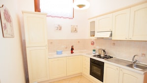 A kitchen with white cabinets, a stove, sink, and a trash bin.