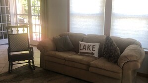 A living room with a beige sofa, a patterned armchair, and a rug. A pillow with "LAKE" is on the sofa. - Beautiful Cabin on Beach Resort in Northern Michigan! (Bellaire)