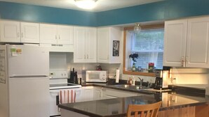 A kitchen with white cabinets, a wooden island with a chair, a refrigerator, a microwave, and a stove. - Beautiful Cabin on Beach Resort in Northern Michigan! (Bellaire)