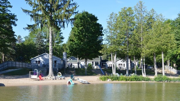 A lakeside cabin with a dock, surrounded by trees and a sandy beach. - Beautiful Cabin on Beach Resort in Northern Michigan! (Bellaire)