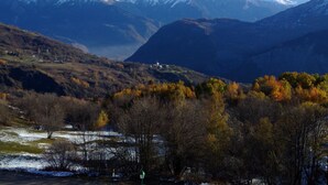 Eine Berglandschaft mit schneebedeckten Gipfeln und herbstlich gefärbten Bäumen.