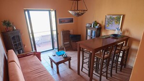 Una sala de estar con sofá, una mesa de comedor con sillas, televisor y ventana con vistas.