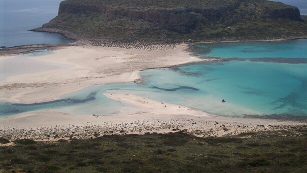 Un paisaje costero con una colina destacada, aguas turquesas cristalinas y una playa de arena.