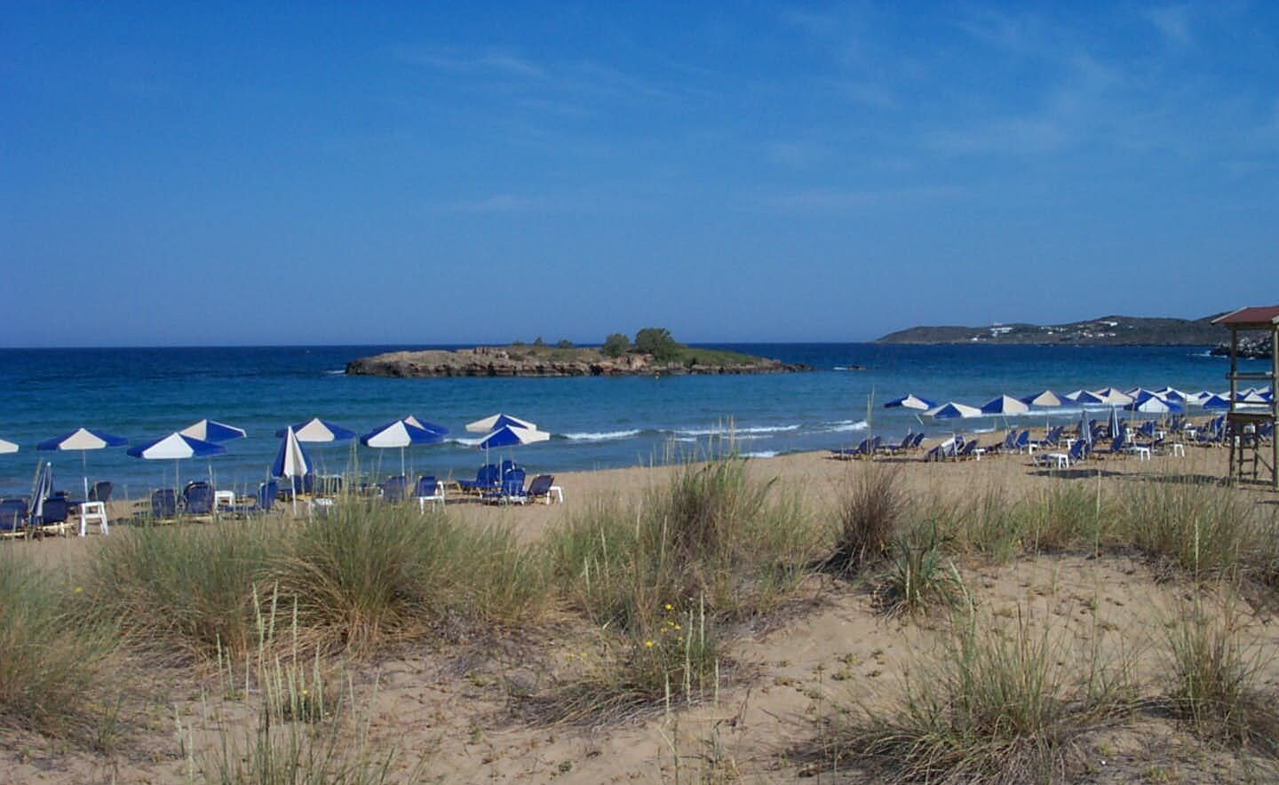 Ein Strand mit Reihen blauer und weißer Sonnenschirme, Liegestühle und einem Rettungsturm.