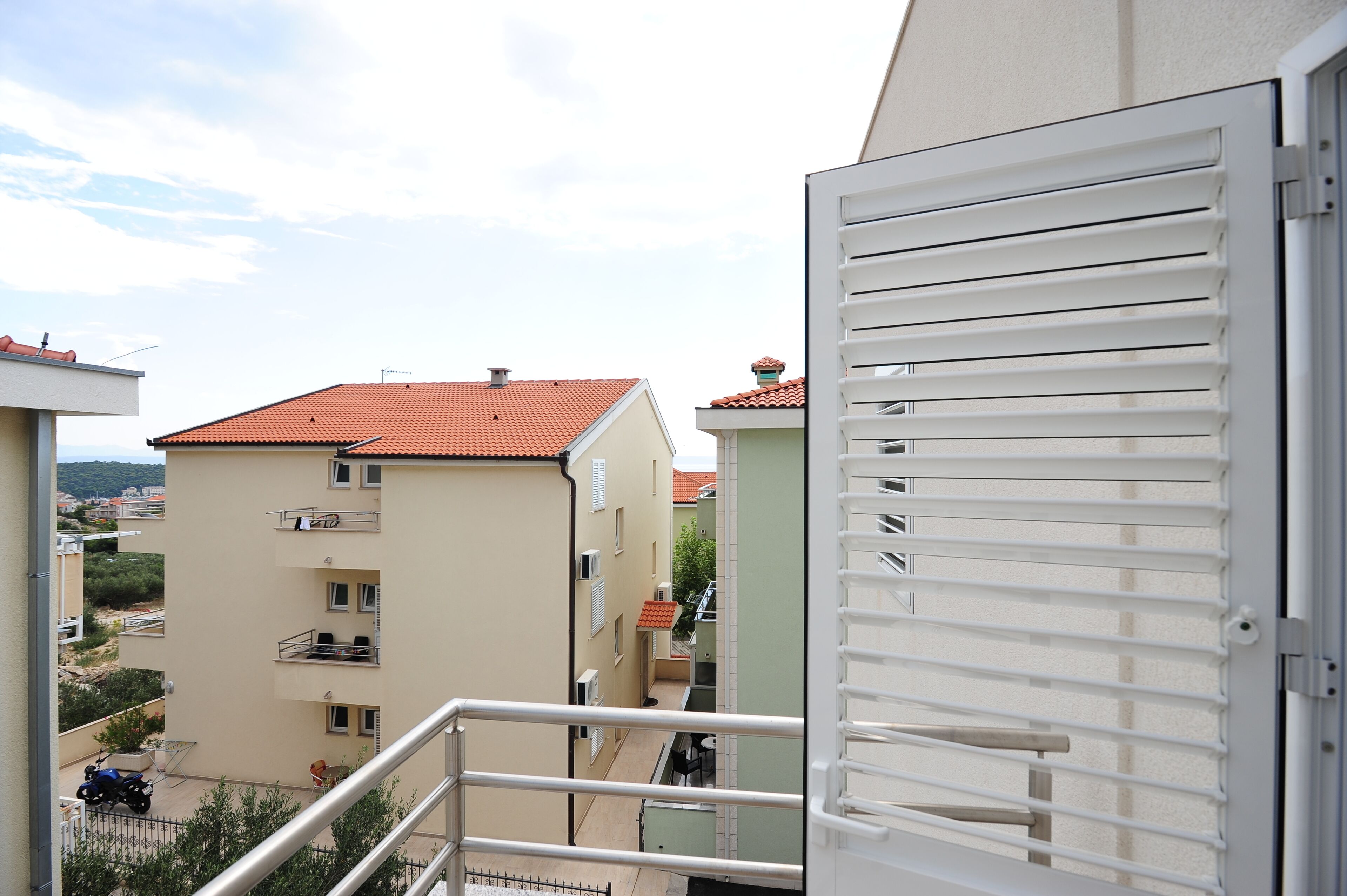 A residential building with a red-tiled roof, balconies, and a view of a neighboring building.