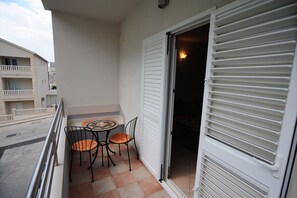 A balcony with a table and chairs, a sliding door, and a view of the street.