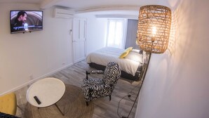 Une chambre à coucher avec un lit, un fauteuil à motifs zébrés, une télévision et une lampe en osier.