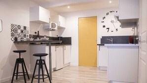 Une cuisine moderne avec des meubles blancs, un four à micro-ondes et deux tabourets noirs.