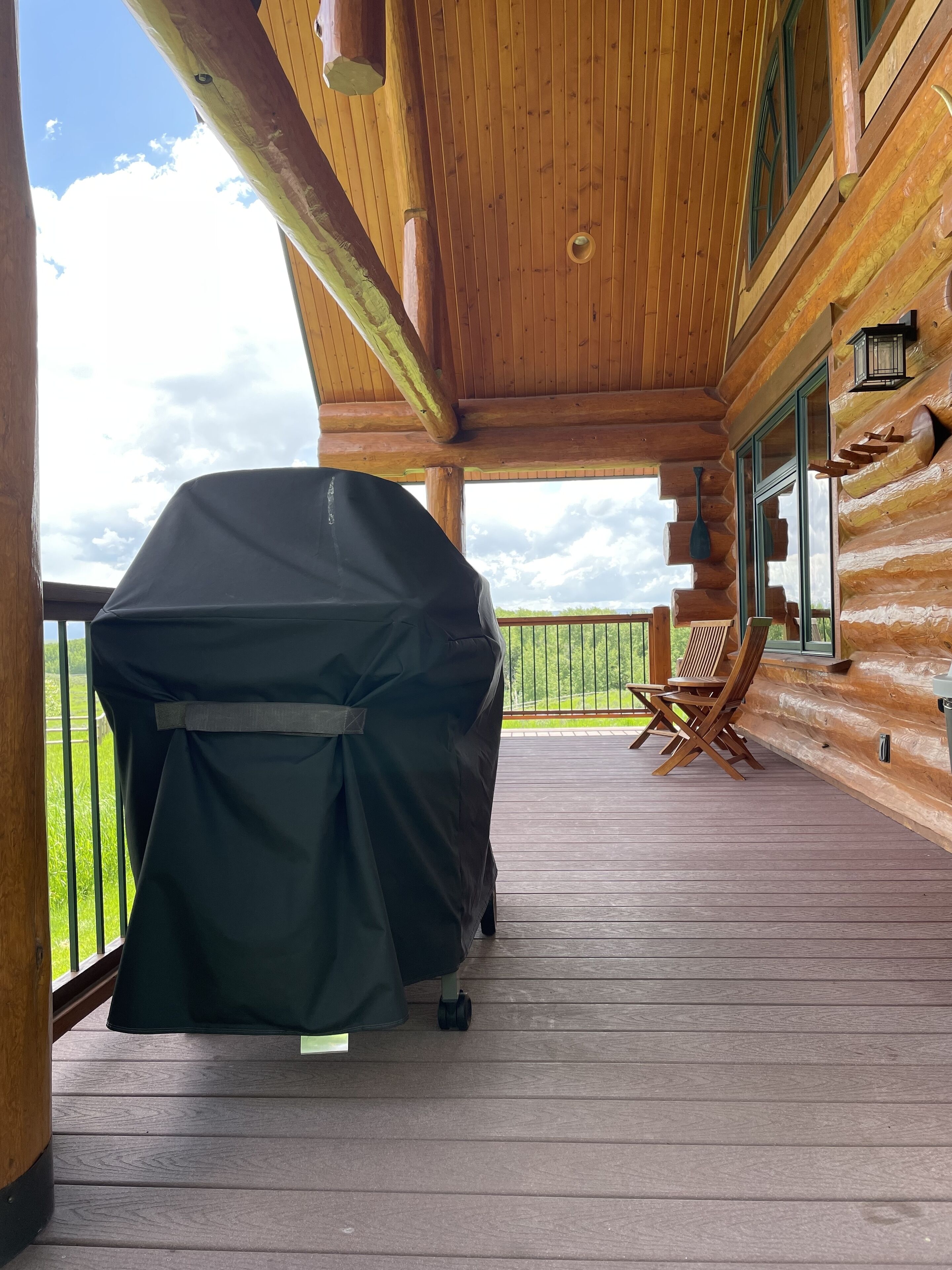 A covered outdoor area with a grill, wooden deck, and a view of the landscape.