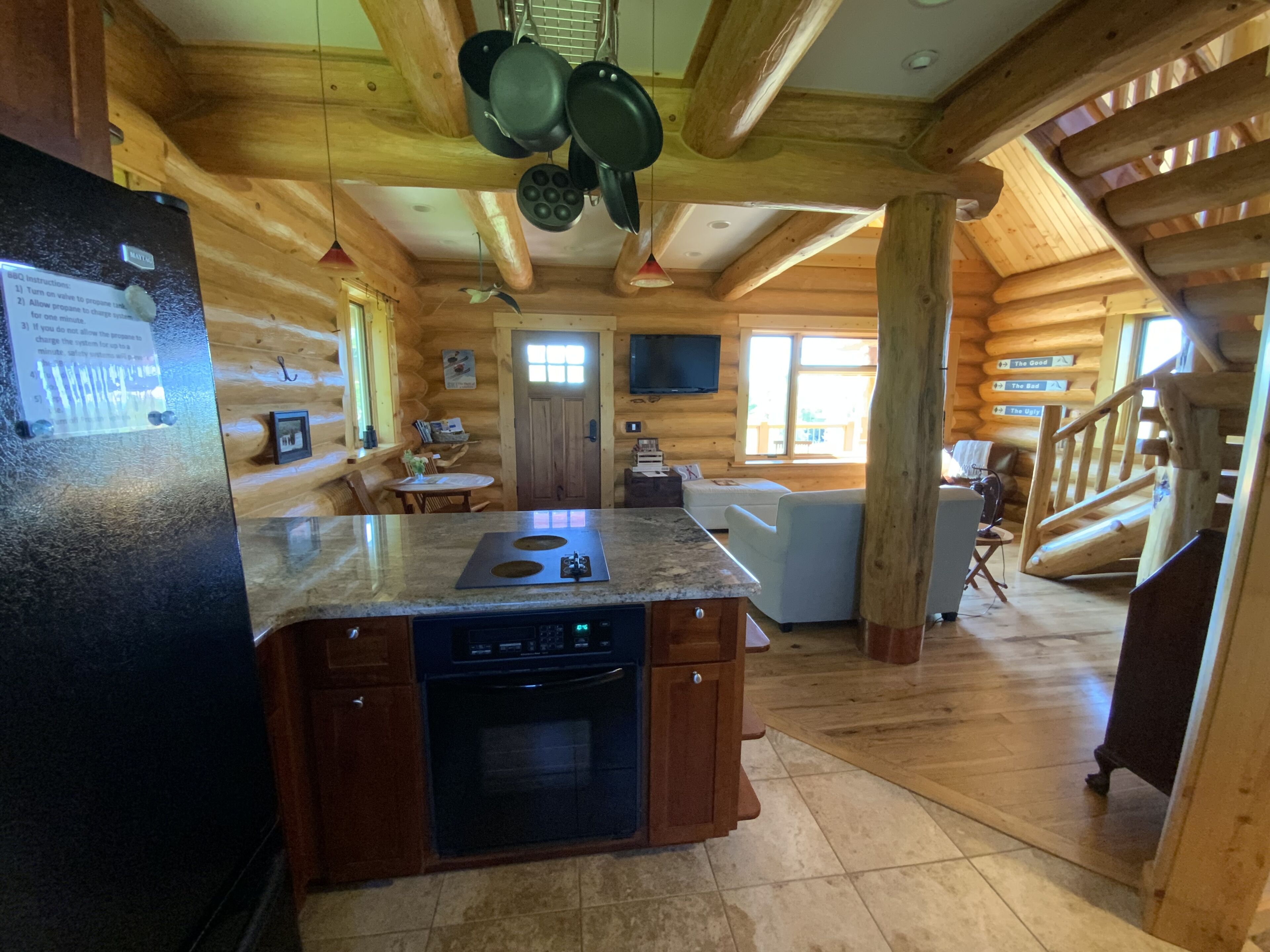 Interior d'una cabana de fusta amb cuina que inclou taulell de granat, rentavaixelles i forn integrat. Hi ha una zona de dinar amb taula i cadires, i una escala que mena a un altre nivell.