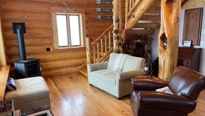 Interior acogedor de una cabaña con chimenea, un sofá, un sillón de cuero y una escalera.