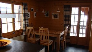 Een houten interieur met een eettafel en stoelen, een kom op het aanrecht en ingelijste foto's aan de muur.