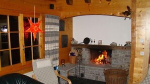 Een gezellige kamer met een open haard, twee stoelen, een tafel en een decoratieve ster aan het plafond.