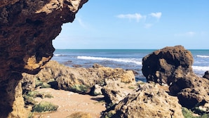 Una playa rocosa con una gran abertura de cueva hacia el mar, rodeada de grandes rocas y piedras.