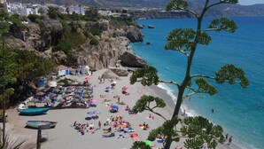 Ein Strand mit vielen Sonnenschirmen und Liegestühlen, felsigen Klippen und freiem Blick auf das Meer.