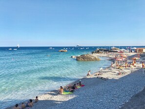 A beach with pebbles, people sunbathing, and boats in the water.
