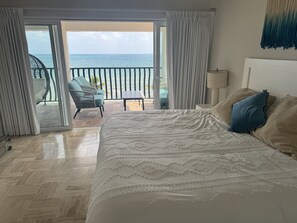 Une chambre d’hôtel avec un grand lit, une vue sur la mer et un balcon équipé de chaises.