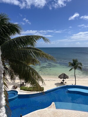 Une vue sur la piscine, avec un ciel bleu dégagé, une plage de sable et une mer calme.