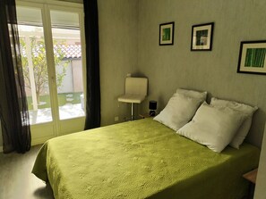 Una habitación de hotel con cama, una silla, una mesita y un ventanal con cortinas.