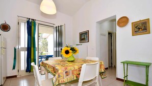 Un coin repas avec une table dressée pour deux personnes, un vase contenant un tournesol et une petite table d’appoint verte.