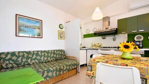 Un espace de vie compact comprenant un canapé, une table à manger agrémentée d’un centre de table en forme de tournesol, un lave-linge et un coin cuisine avec des placards et une cuisinière.