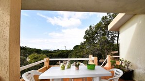 Une table et des chaises blanches sur un balcon, avec vue sur des arbres et une montagne lointaine.
