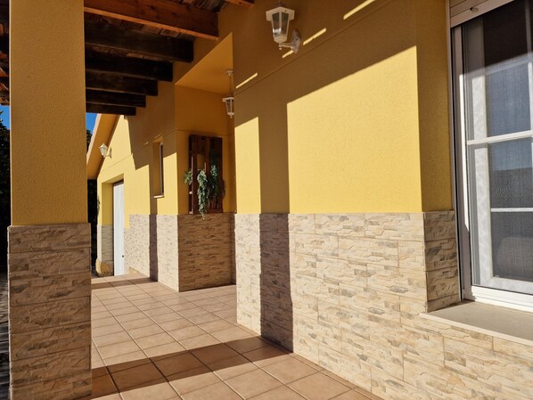 A covered outdoor area with stone pillars, yellow walls, and a tiled floor.