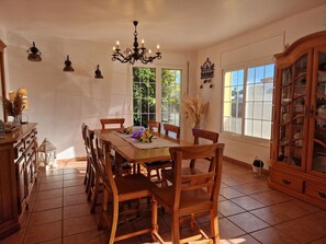 A dining room with a wooden table, chairs, a chandelier, and a cabinet with glass doors.
