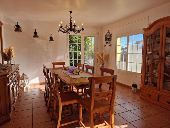 A dining room with a wooden table, chairs, a chandelier, and a cabinet with glass doors.