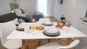 Un coin repas avec une table blanche dressée pour le petit-déjeuner, comprenant des assiettes, des verres et une machine à café.