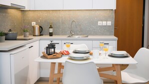 Une cuisine moderne avec des meubles blancs, un plan de travail, un évier et un coin repas avec une table mise pour deux personnes.