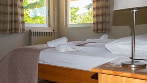 A neatly made bed with white linens and a beige throw blanket, a bedside table with a lamp, and a window with curtains. - Studio on the sunset beach (Attiki)