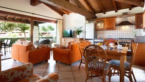 Ein großzügiger Wohnbereich mit orangefarbenen Sofas, einem Esstisch mit Stühlen und einer Küche mit Holzausziehtischen und einer gefliesten Spritzschutzwand.
