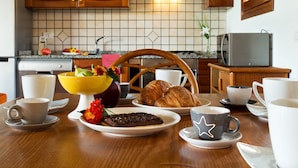 Ein Frühstückstisch mit Holzplatte, verschiedenen Tassen, einer Fruchtschale, einem Croissant und einem Schokoladenkuchen.