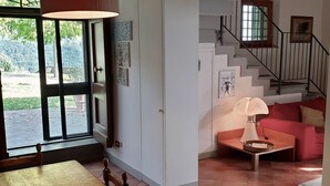 Un salon spacieux avec une table en bois, un canapé rouge, un escalier et une vue sur la verdure à l’extérieur.