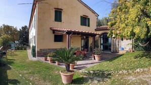 Une maison à deux étages, avec un toit en tuiles, une terrasse couverte et un jardin agrémenté de plantes en pot.