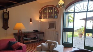 Un salon avec un canapé rouge, un fauteuil blanc, une table en bois et une lampe. Une grande fenêtre offre une vue sur l’extérieur.