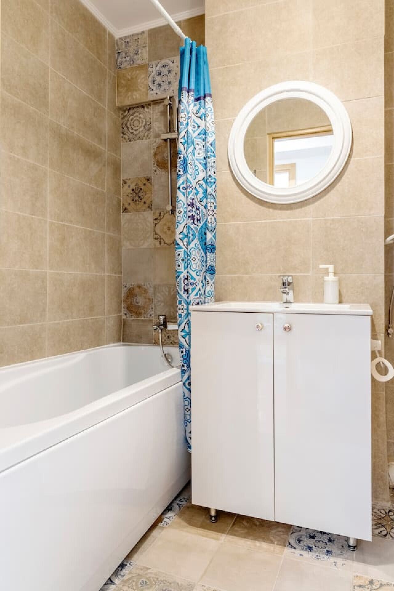 Une salle de bain avec une baignoire blanche, un meuble blanc avec un miroir au-dessus, et des carreaux décoratifs sur les murs.