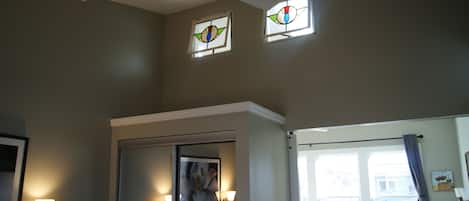 A room with a ceiling fan, two windows with stained glass, a framed artwork, and a door.