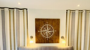 A neatly made bed with striped pillows, a compass wall art, and a tufted headboard. - The Loft: Amazing views, parking & fantastic location! (Kingswear)