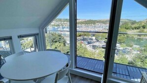 A room with a round table and chairs, large windows offering a view of a marina and surrounding landscape. - The Loft: Amazing views, parking & fantastic location! (Kingswear)